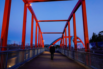 Stockholm, Sweden,  A man walks alone on a red pedestrian and bicycle bridge the suburb of Vastberga.