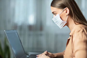 Woman wearing face mask and working on laptop