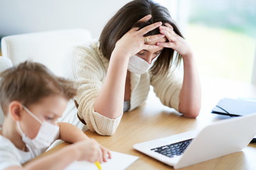 Boy and exhausted mother trying to work at home during coronavirus pandemic