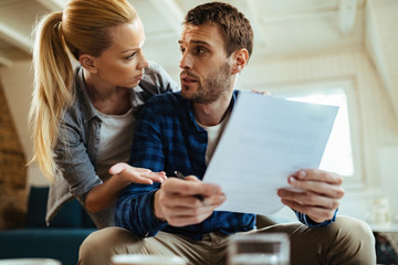 Young displeased couple talking about their financial difficulties at home.