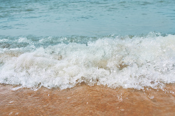 Sandy beach with waves from the sea. Ocean water close up.