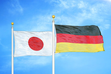 Japan and Germany two flags on flagpoles and blue cloudy sky