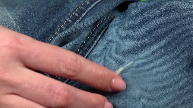 Closeup view 4k video of hole in blue jeans. Female fingers touching texture of blue torn denim pants.
