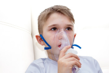 Little boy having inhalation for easing cough. Caucasian blonde boy inhales couples containing...