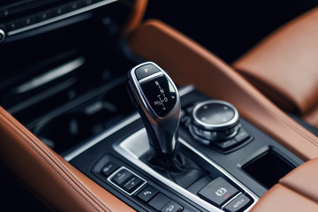 Selector automatic transmission with leather in the interior of a modern expensive car. The background is blurred. Black and brown leather car interior. Luxurious car instrument cluster. Close up shot