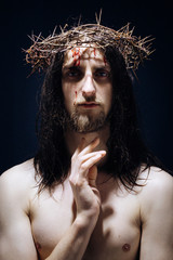 Jesus Christ of Nazareth with crown of thorns looks at people. Closeup portrait