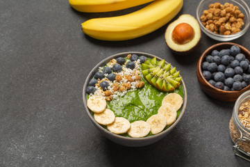 Healthy smoothie in the bowl from avocado and spinach with blueberries, mulberry, banana, granola, coconut and kiwi. Delicious breakfast.