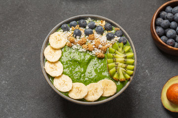 Healthy smoothie in the bowl from avocado and spinach with blueberries, mulberry, banana, granola, coconut and kiwi. Delicious breakfast.