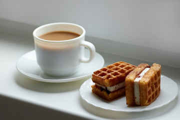 Two pieces of tasty Viennese waffles with cream on a plate with a cup of fresh coffee in the background by the window