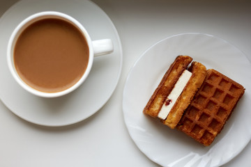 Top view: two pieces of Viennese waffles with cream on a plate with a cup of fresh coffee in the background by the window
