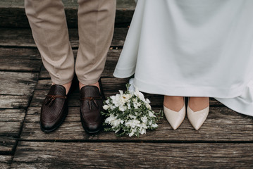 legs of newlyweds on wooden background. stylish shoes of bride and groom outdoors. bridal bouquet on brige close up. .