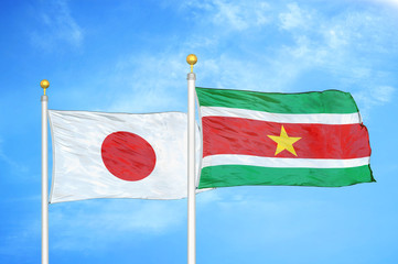Japan and Suriname two flags on flagpoles and blue cloudy sky