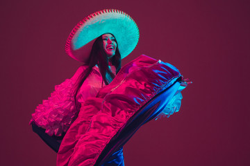 Fabulous Cinco de Mayo female dancer on purple studio background in neon light. Beautiful female model in traditional costume and sombrero dancing. Celebration, holiday, beauty and fashion concept.