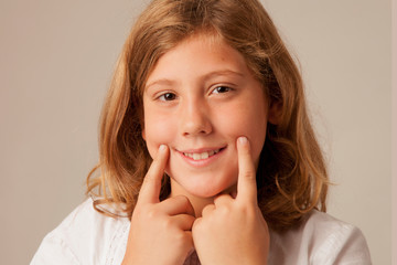 Fototapeta premium Put a smile on face! Portrait of beautiful young girl holding fingers on his mouth and making fake smile.