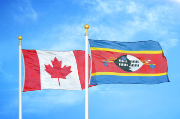 Canada and Eswatini Swaziland two flags on flagpoles and blue cloudy sky
