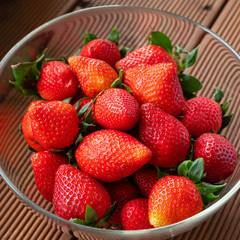 ripe strawberries in a glass dish on a wooden table