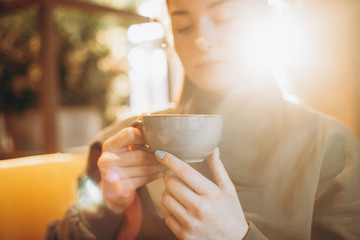young pretty girl with a big mug of sweet coffee sits on a chair in her favorite cafe and drinks her daily morning coffee and talks with a girlfriend