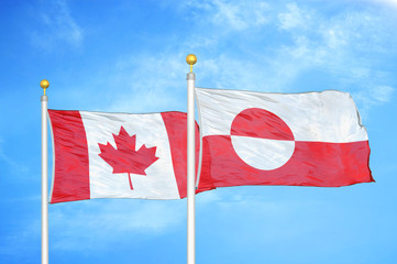 Canada and Greenland two flags on flagpoles and blue cloudy sky