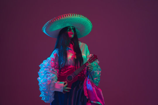 Fabulous Cinco de Mayo female dancer on purple studio background in neon light. Beautiful female model in traditional costume and sombrero dancing. Celebration, holiday, beauty and fashion concept.