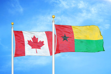 Canada and Guinea-Bissau two flags on flagpoles and blue cloudy sky