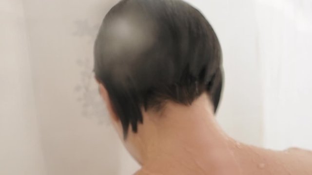 Naked woman takes a shower. Woman washes her short hair . Slow motion video in white bathroom.