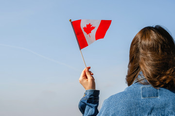 Fototapeta na wymiar Woman hand with Canada swaying flag on the blue sky. America. USA. Concept