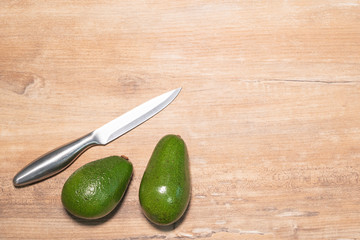 Two ripe avocados and a silver knife on a wooden background, a place for your text