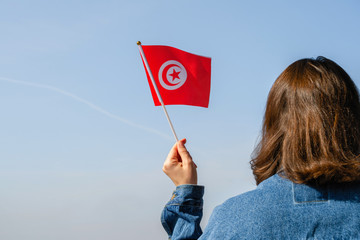 Muslim woman with Tunisia flag on the blue sky. Concept