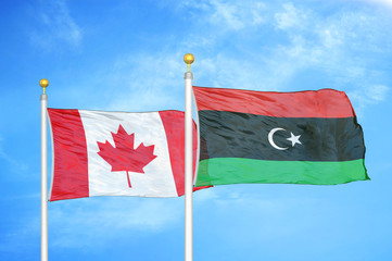 Canada and Libya two flags on flagpoles and blue cloudy sky