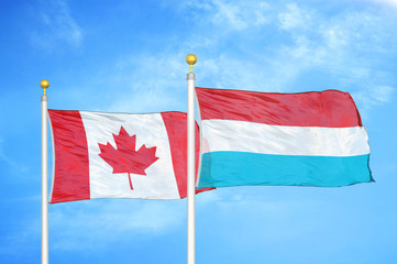 Canada and Luxembourg two flags on flagpoles and blue cloudy sky