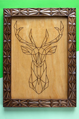 Wooden picture with the image of a deer made using the technique of pyrography and decorated with a carved frame