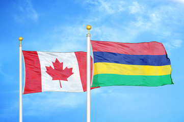 Canada and Mauritius two flags on flagpoles and blue cloudy sky