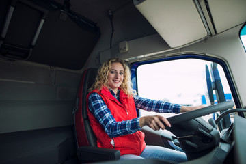 Portrait of trucker sitting in truck cabin with hands on steering wheel.