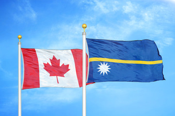 Canada and Nauru two flags on flagpoles and blue cloudy sky