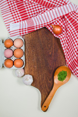 Wooden cutting board with red rug, spices, ladle, eggs and garlics