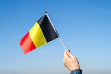 Woman hand with Belgian swaying flag on the blue sky. Belgium. Concept - obrazy, fototapety, plakaty