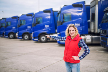 Female trucker standing in front of parked trucks and pointing her finger to the transportation...