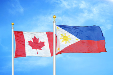 Canada and Philippines two flags on flagpoles and blue cloudy sky