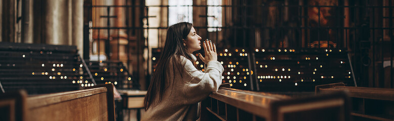 a young pretty woman came to the temple to pray to God. The parishioner of the church sits on a bench with her hands folded for prayer and heartily prays. copy space - Powered by Adobe