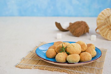 Fototapeta na wymiar Ball-shaped sweet coconut cookies on a blue clay plate on a light concrete background. Coconut Baking. Copy space.