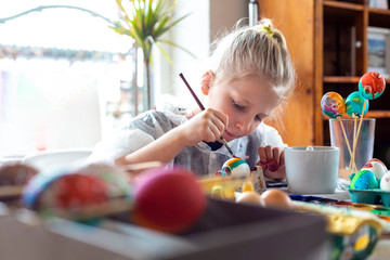 Portrait of adorable blonde girl at home painting easter eggs