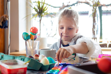 Portrait of adorable blonde girl at home painting easter eggs
