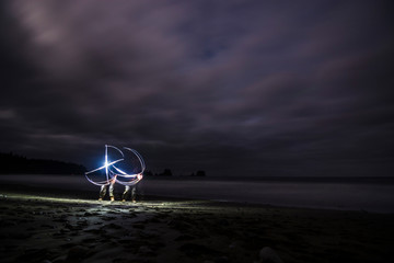 Adventurous man light painting on a sandy beach at night.