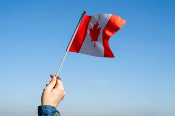 Fotobehang Woman hand with Canada swaying flag on the blue sky. America. USA. Concept © flowertiare