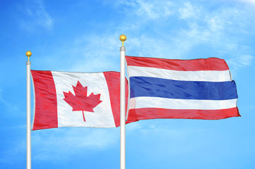 Canada and Thailand two flags on flagpoles and blue cloudy sky