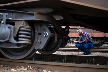 Railroad worker inspecting wheels and brakes of the freight train. Safety inspector checking...