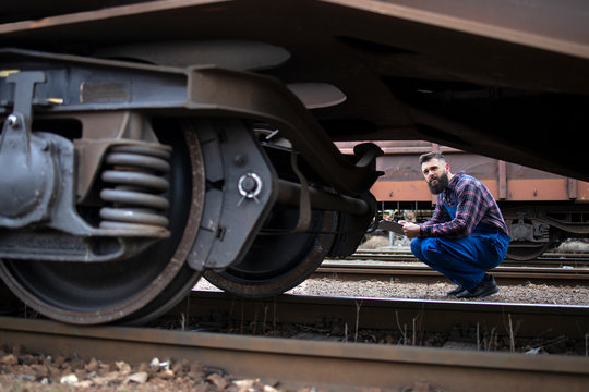 Railroad worker inspecting wheels and brakes of the freight train. Safety inspector checking transportation vehicle and railway tracks before departure.