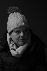 Lady closeup headshot portrait. She is in her 40s, has long smooth black hair. She is wearing winter clothes. She is looking to the side. This is a black and white image.