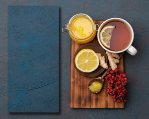 Fototapeta na wymiar Lemon honey and ginger on wooden plate with a cup of hot tea background. Top view, mockup, flat lay. Season illness prevention. Background with copy space and design mockup.