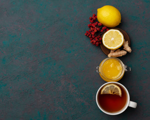 Obraz na płótnie Canvas Season illness prevention background. Vitamin tea with lemon, ginger and honey with rowanberry on dark green wooden background.